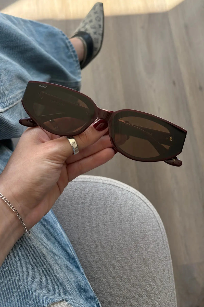 Hand holding Astra sunglasses in Black Cherry Red in a close-up lifestyle photo.