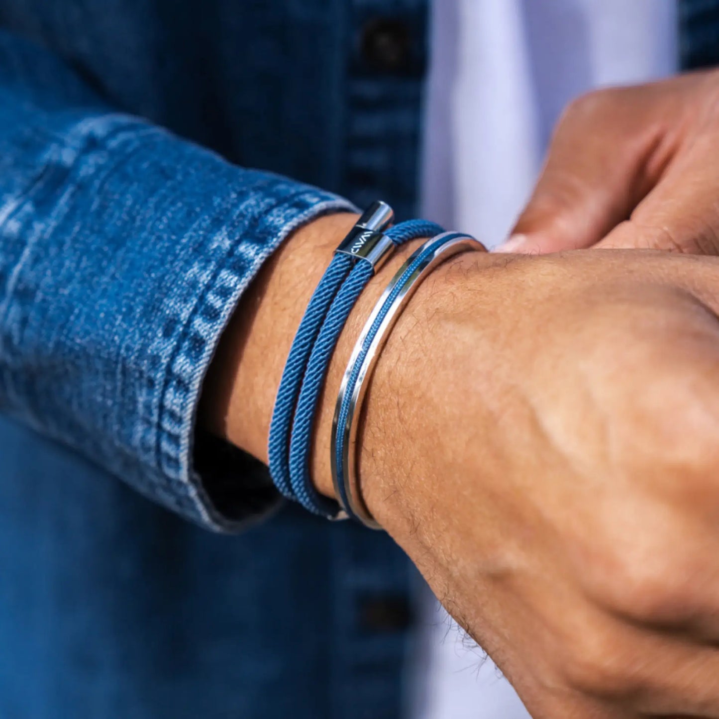 Blue rope bracelet with polished silver tube clasp paired with slim silver bangle on wrist in denim shirt sleeve