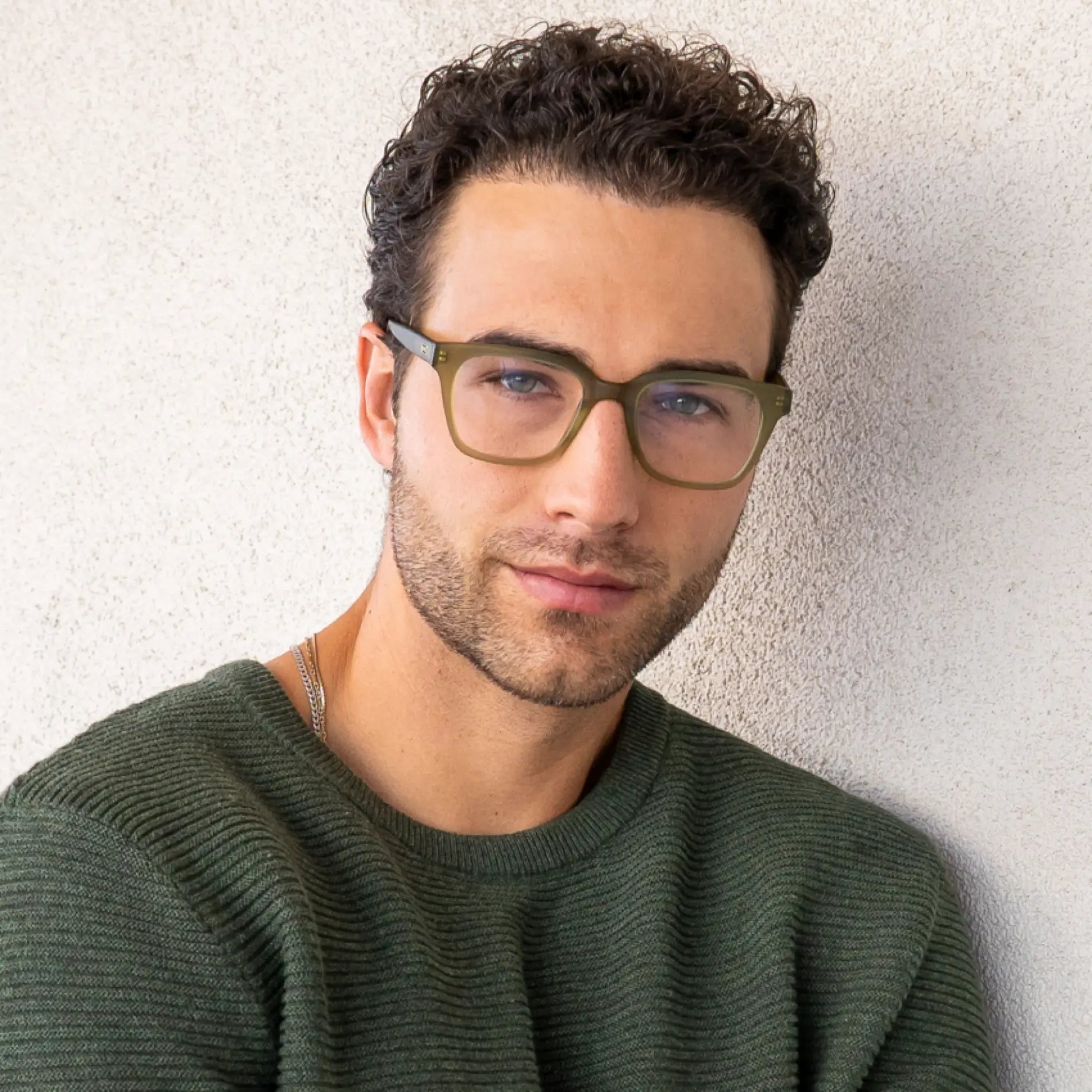 Frosted Khaki Green || Blue Light rectangular khaki green frames on man with curly hair against textured wall