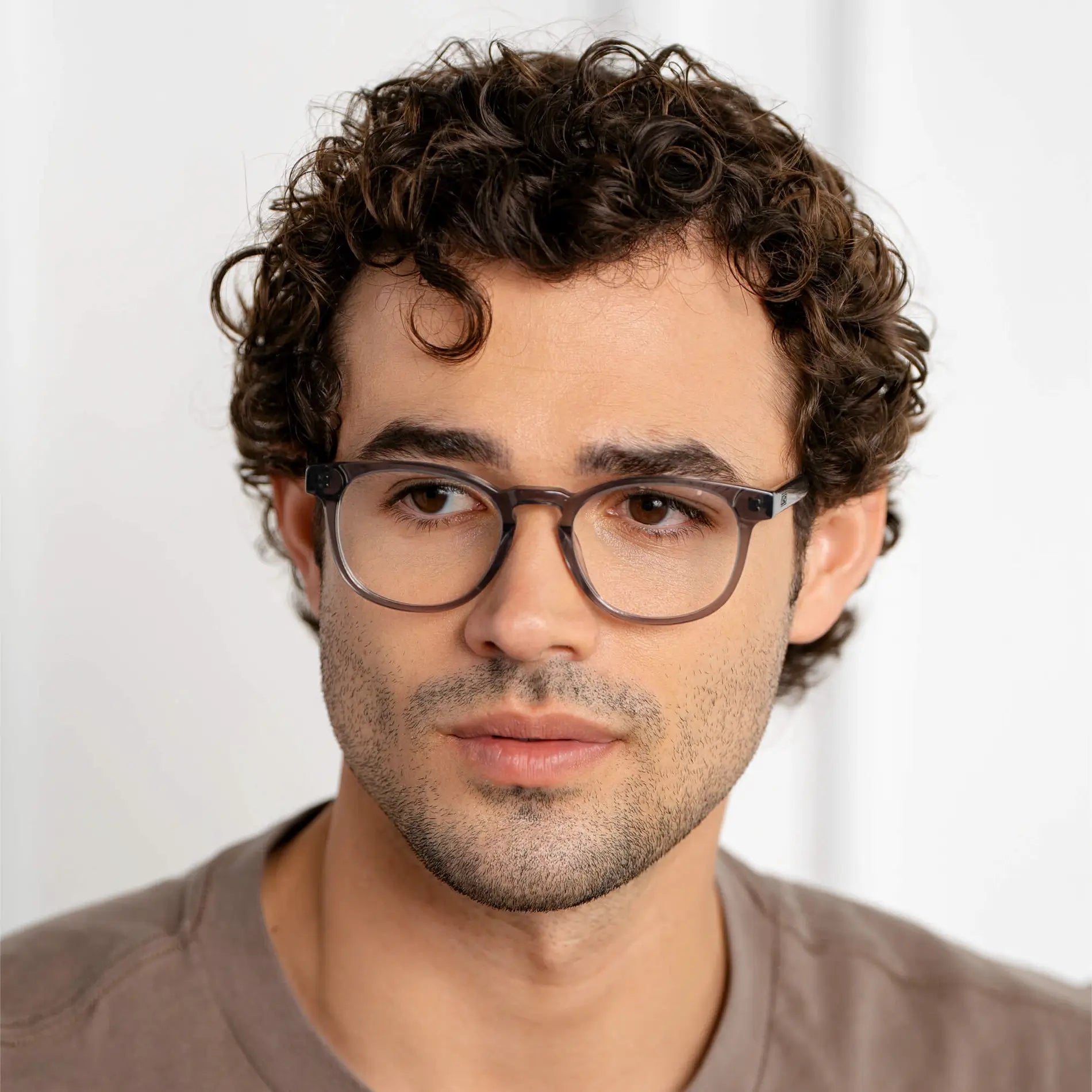 Crystal Grey || Cal blue light glasses featuring translucent grey square frames worn by man with curly hair in soft lighting