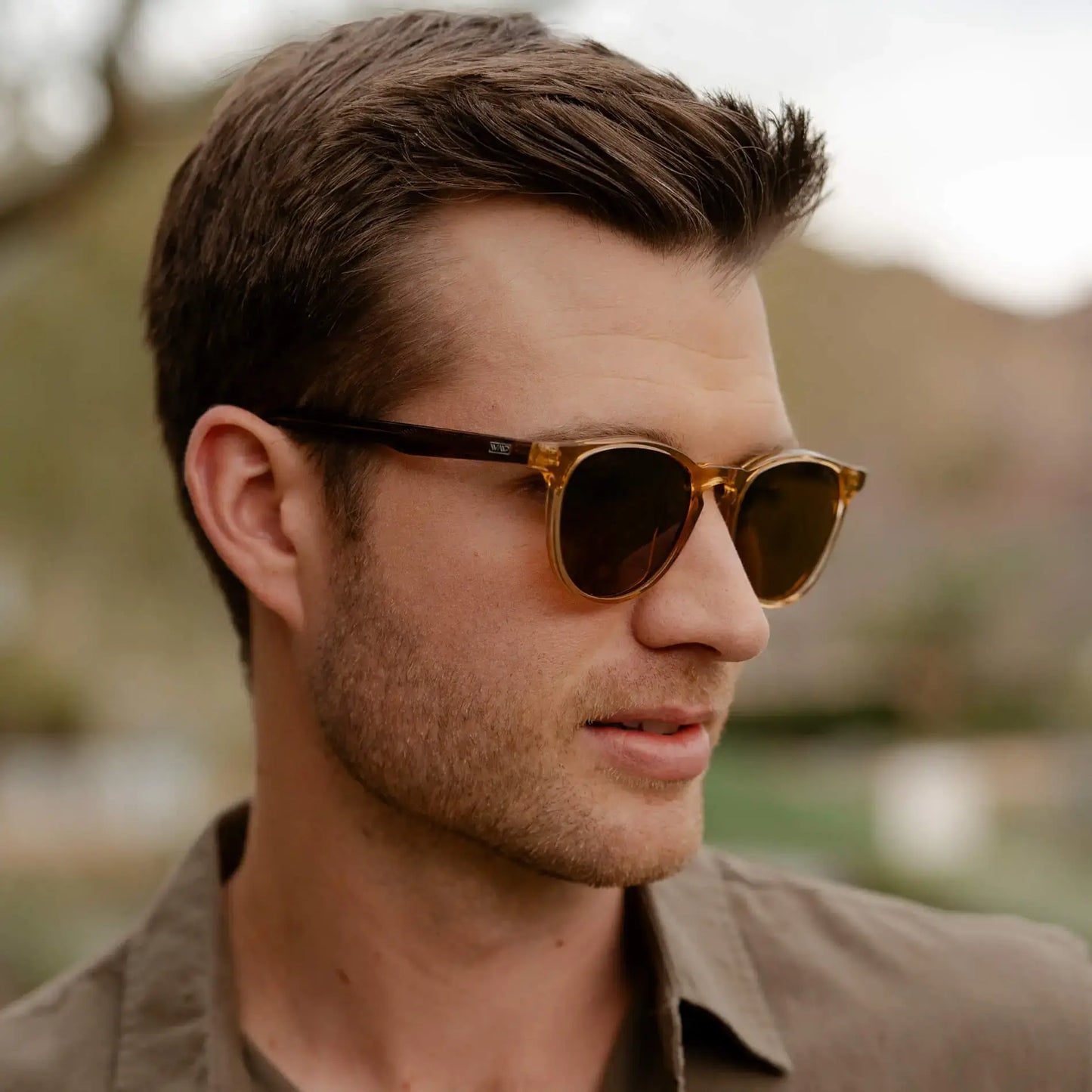 Crystal Brown Marble / Amber || Round modern prescription sunglasses with crystal brown marble acetate frame and keyhole bridge worn by man outdoors
