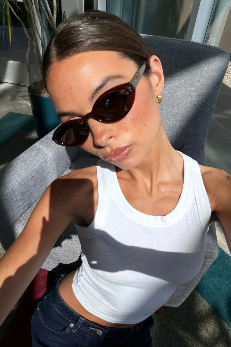 Woman wearing WMP Eyewear oval sunglasses in deep burgundy red with dark lenses