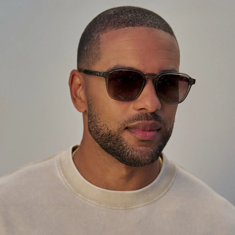 Model wearing WMP Eyewear Francis sunglasses in Sage Green, featuring a translucent green-gray frame with brown gradient lenses.