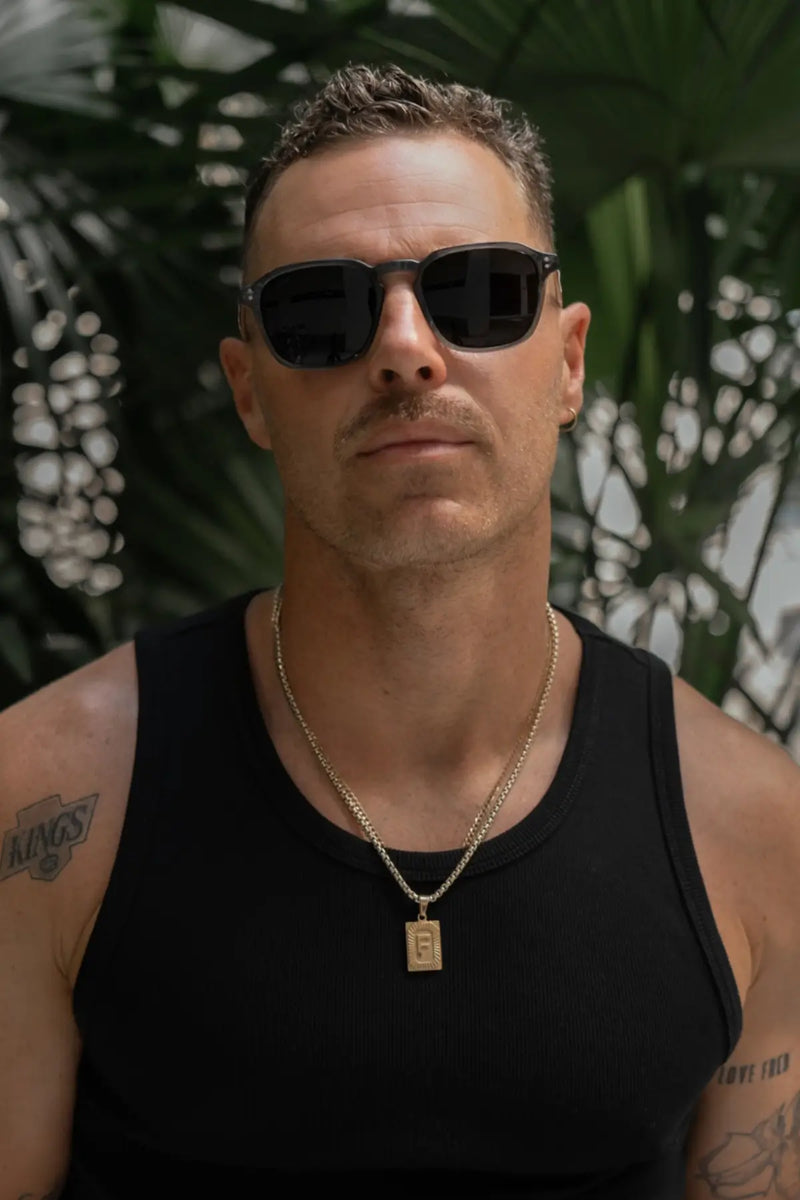 Close-up of a model wearing Francis sunglasses in Crystal Stone Blue in an outdoor lifestyle setting with tropical plants.