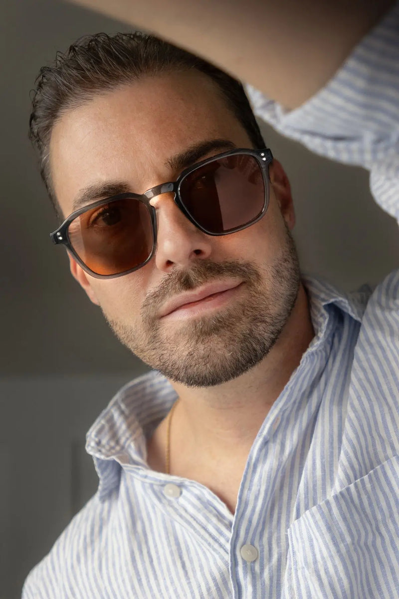 Man wearing geometric crystal stone blue-frame WMP Francis sunglasses with brown lenses, striped button-down shirt, close-up selfie style