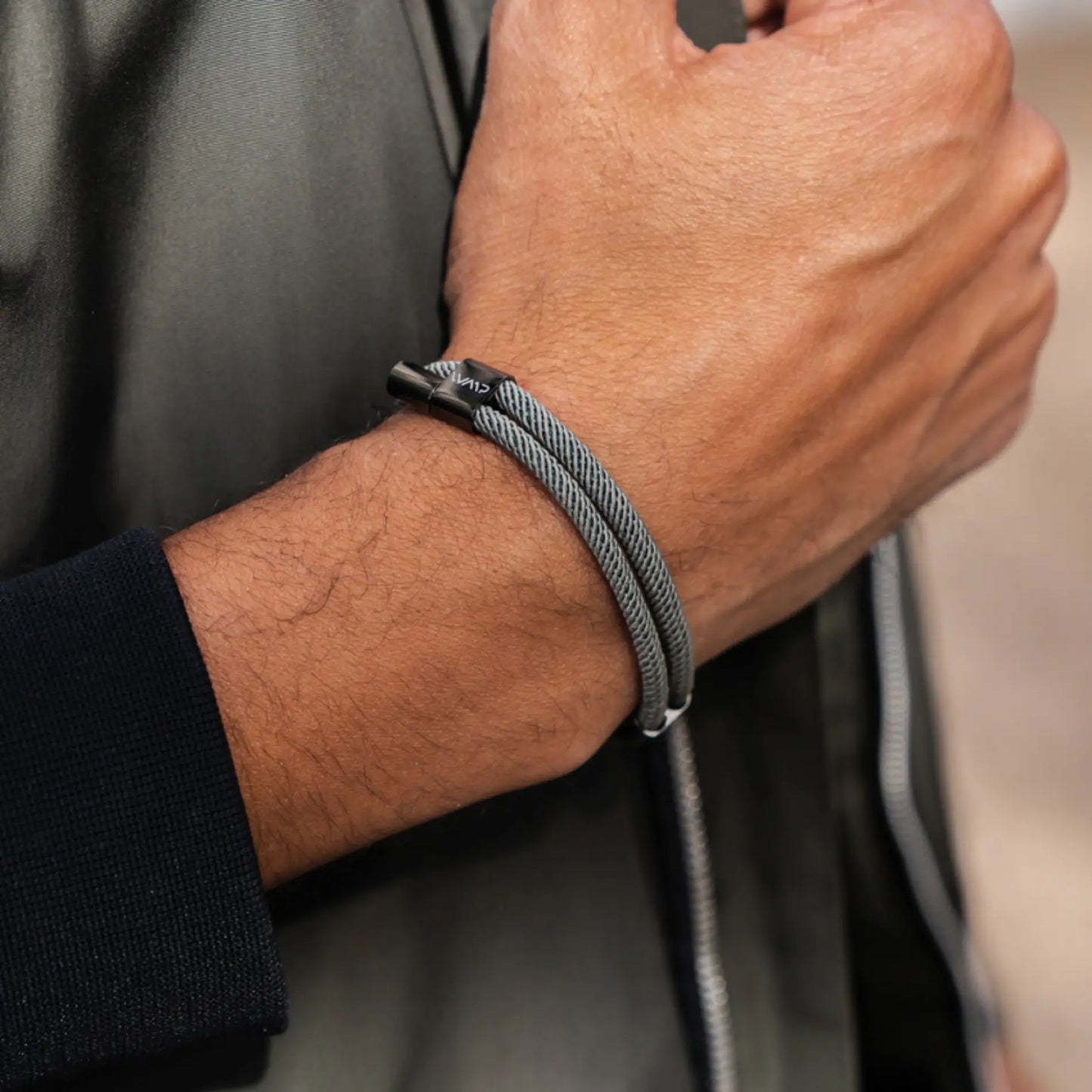 Olive Green / Gunmetal || Grey twisted rope bracelet featuring black polished clasp on wrist against dark clothing background