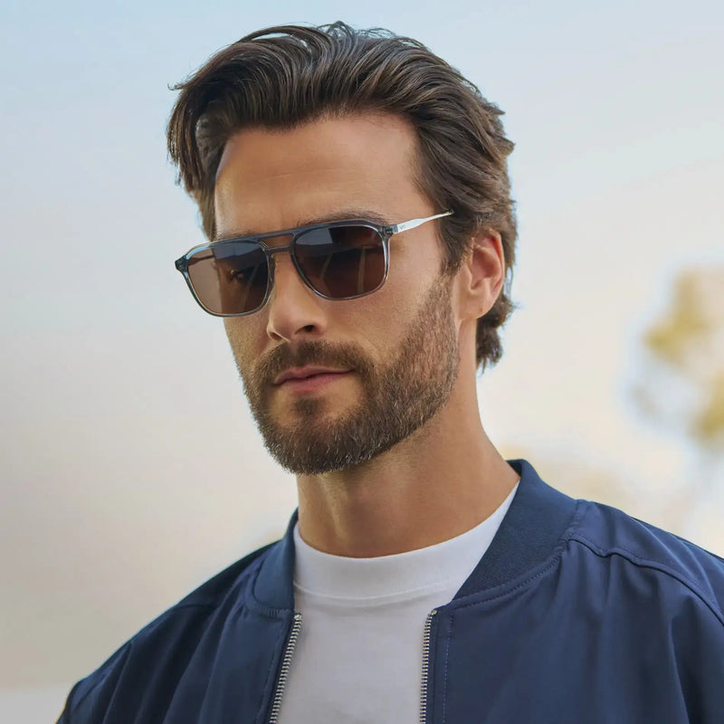 Model wearing Gage sunglasses in Blue in a side-profile outdoor lifestyle photo with a blurred background.