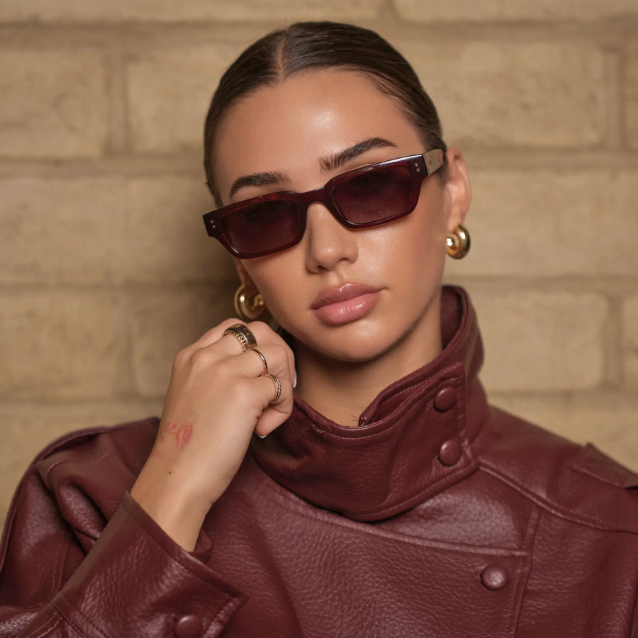 Model wearing WMP Eyewear Harper sunglasses in Red Garnet, featuring a narrow angular frame with brown gold gradient lenses.