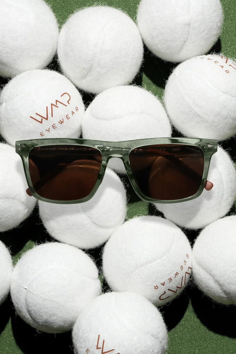 WMP Eyewear Hart sunglasses in transparent green with brown lenses, resting on branded tennis balls