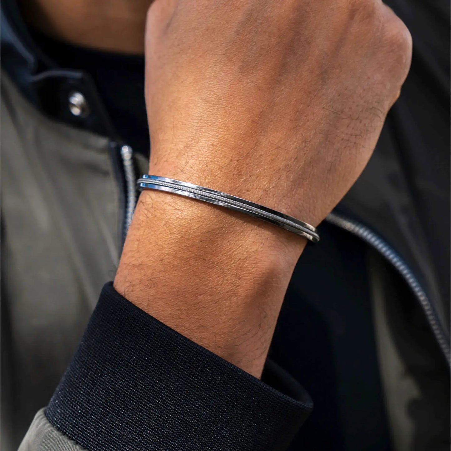 Gunmetal / Olive Green || Close up of wrist wearing a slim polished silver Kent bracelet with textured detail on dark background