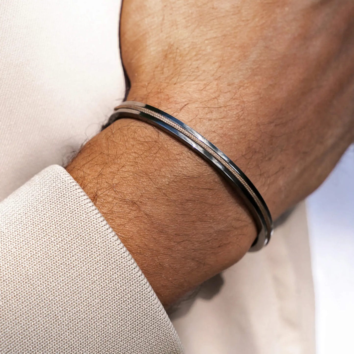 Gunmetal / Sand Rope || Man’s wrist wearing a slim polished Kent bracelet with subtle black detailing against light beige fabric background
