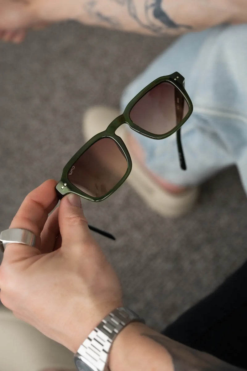 Close-up of a hand holding Morris sunglasses in Jade Green with a softly blurred background.