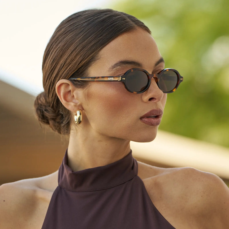 Woman wearing WMP Eyewear round tortoiseshell sunglasses with dark brown lenses