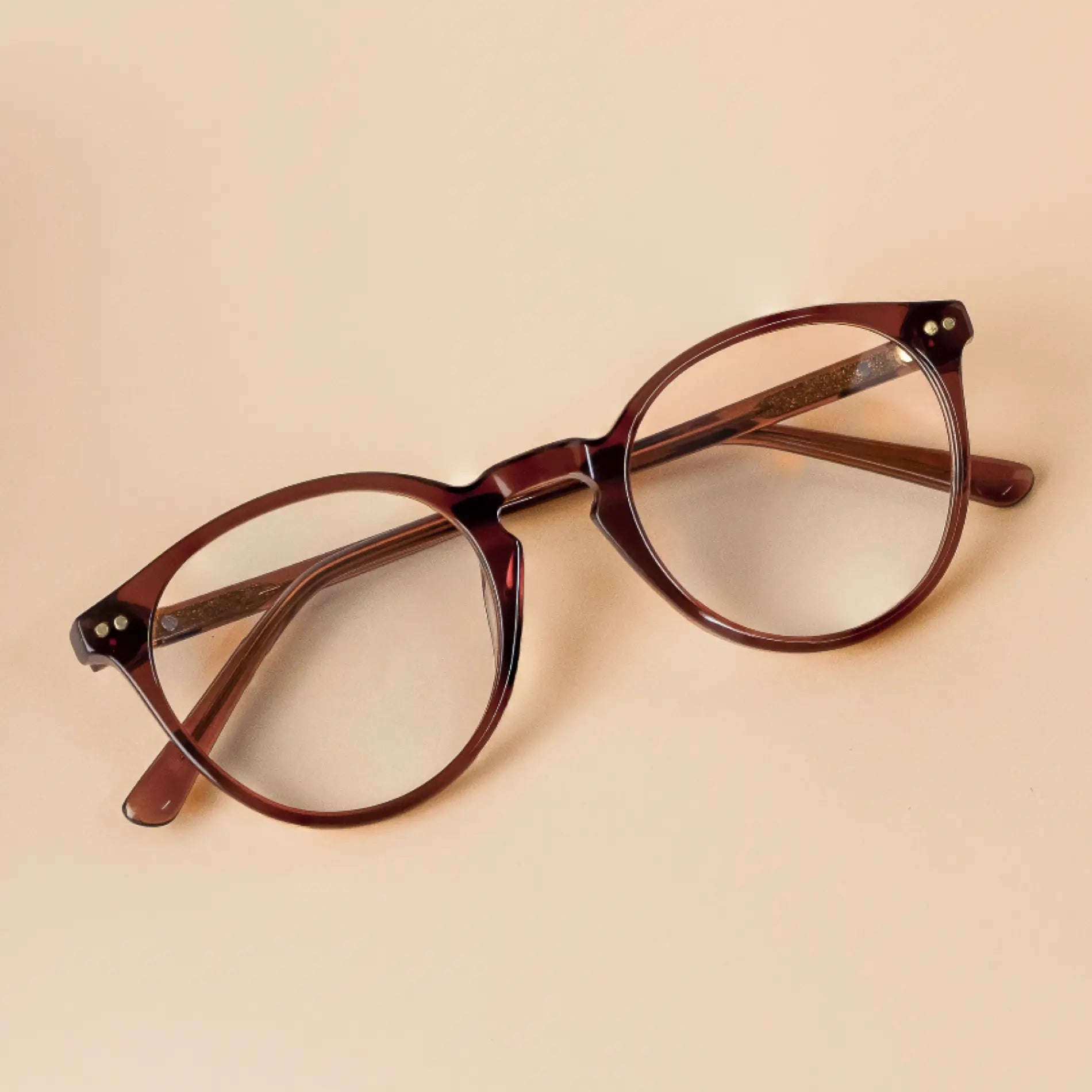 Crystal Chestnut Brown || Owen blue light glasses with translucent rounded brown frames resting on beige surface