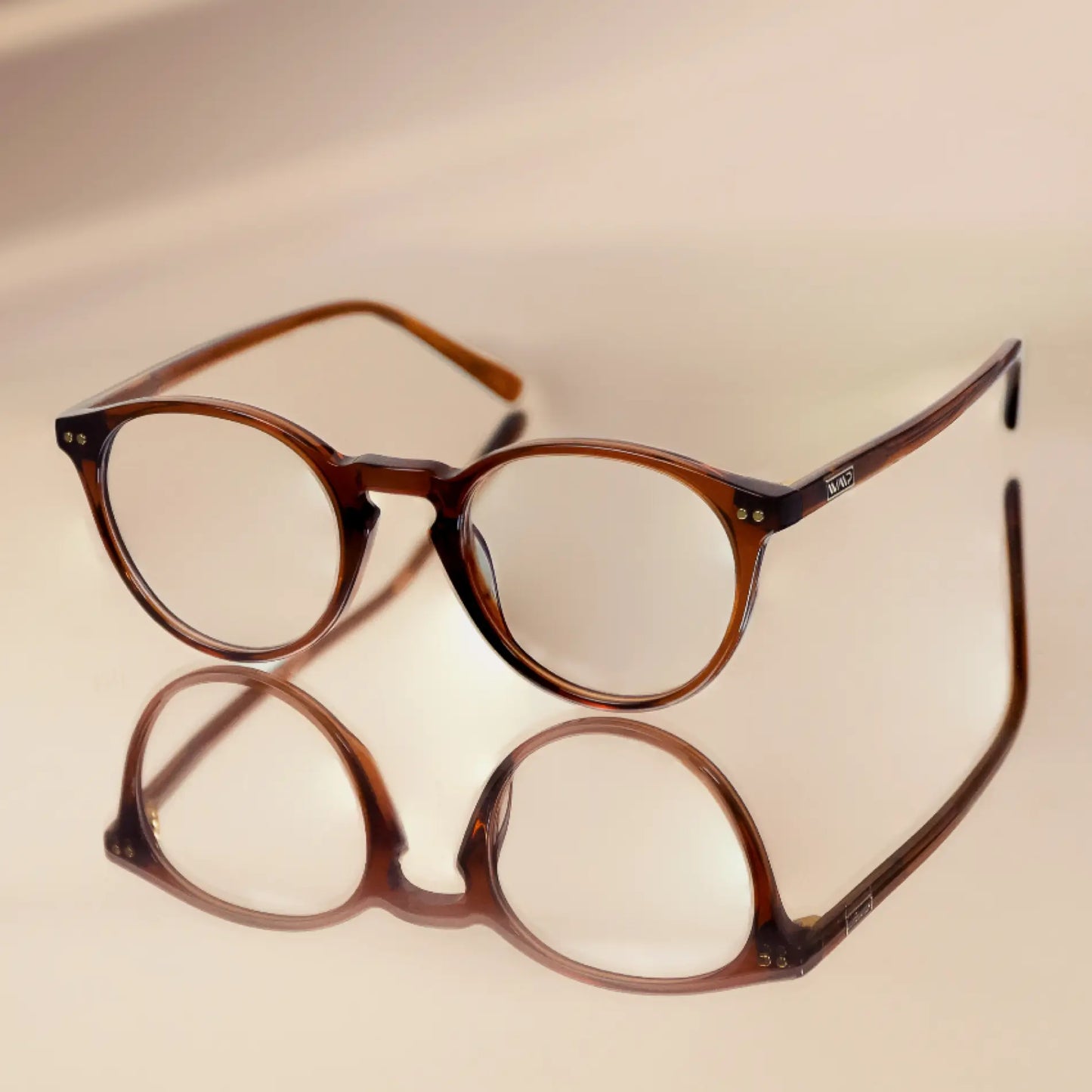 Crystal Chestnut Brown || Blue light glasses with translucent brown round frames resting on reflective surface against beige background