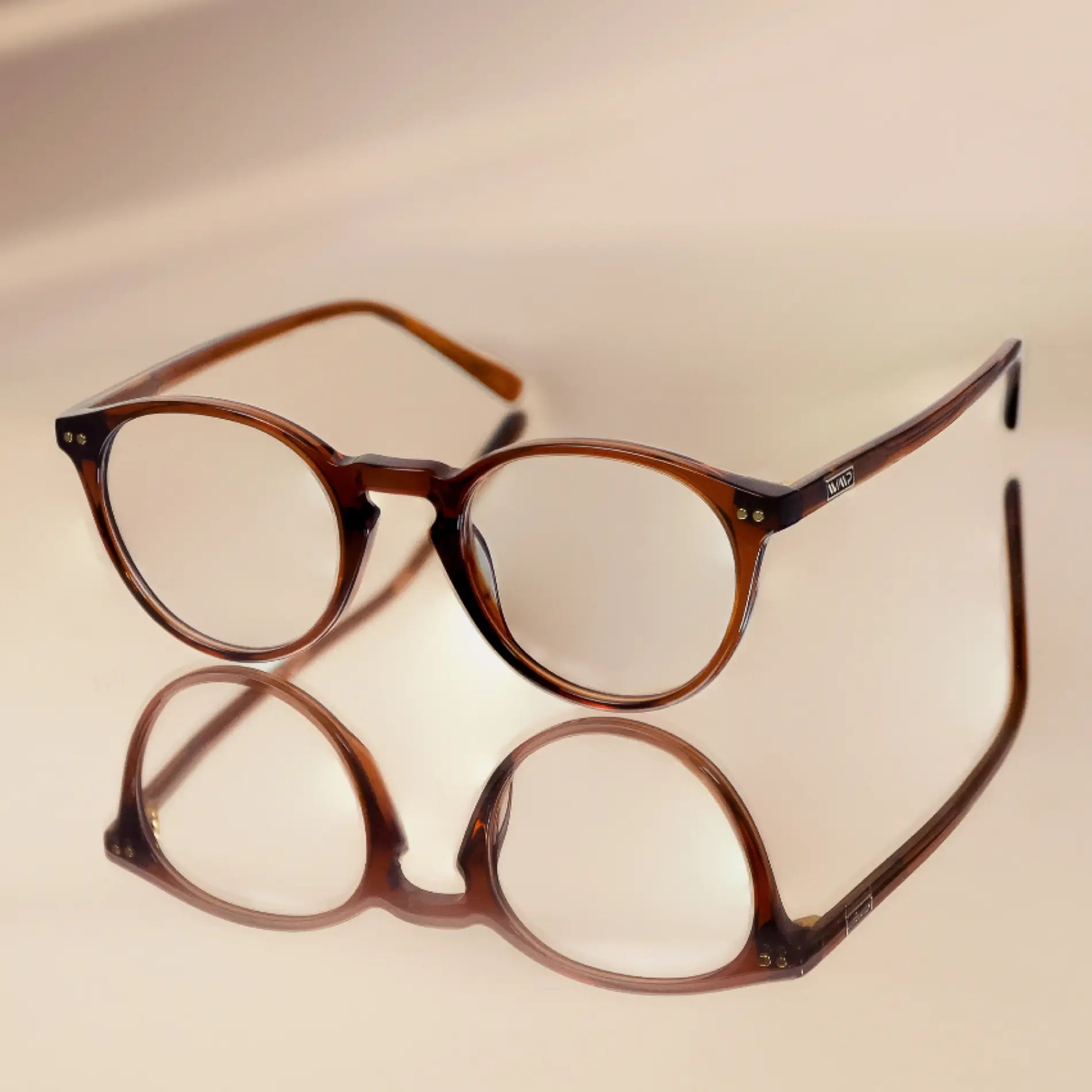 Crystal Chestnut Brown || Blue light glasses with translucent brown round frames resting on reflective surface against beige background
