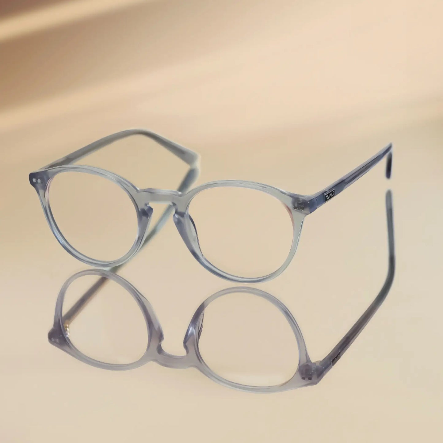 Cloudy Grey || Blue light glasses with translucent rounded frames resting on reflective beige surface