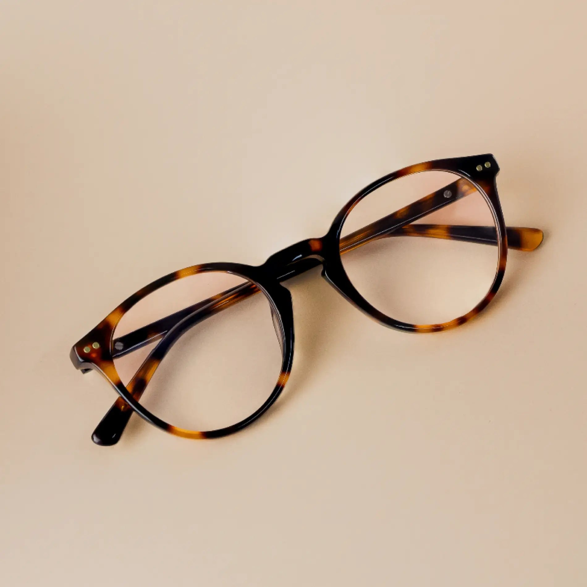 Tortoise Brown || Owen blue light glasses with tortoise shell rounded frames resting on beige surface against neutral background