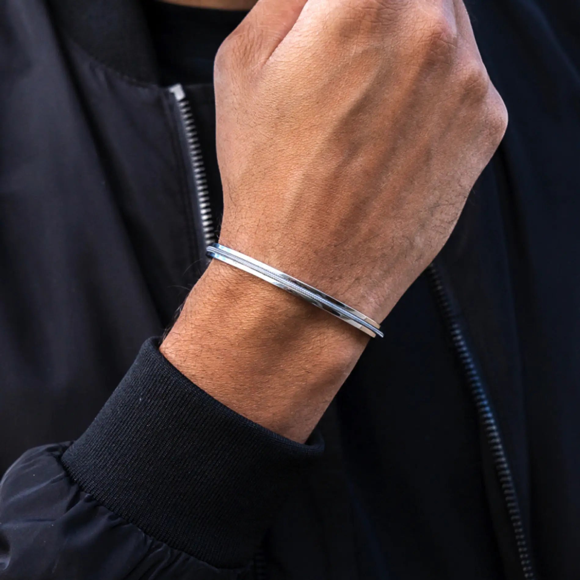 Stone Grey / Silver || Polished silver slim cuff bracelet worn on wrist over black jacket sleeve and dark shirt background