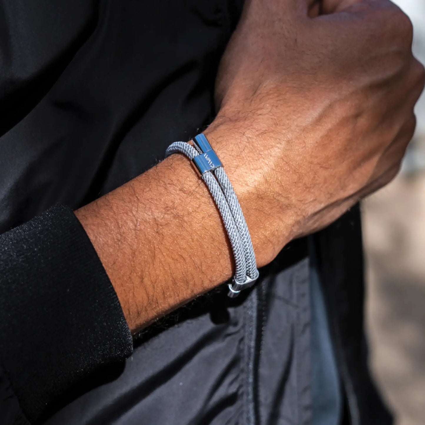 Stone Grey / Silver || Close up of wrist wearing a sleek silver braided Knox Bracelet with metal clasp against black jacket sleeve