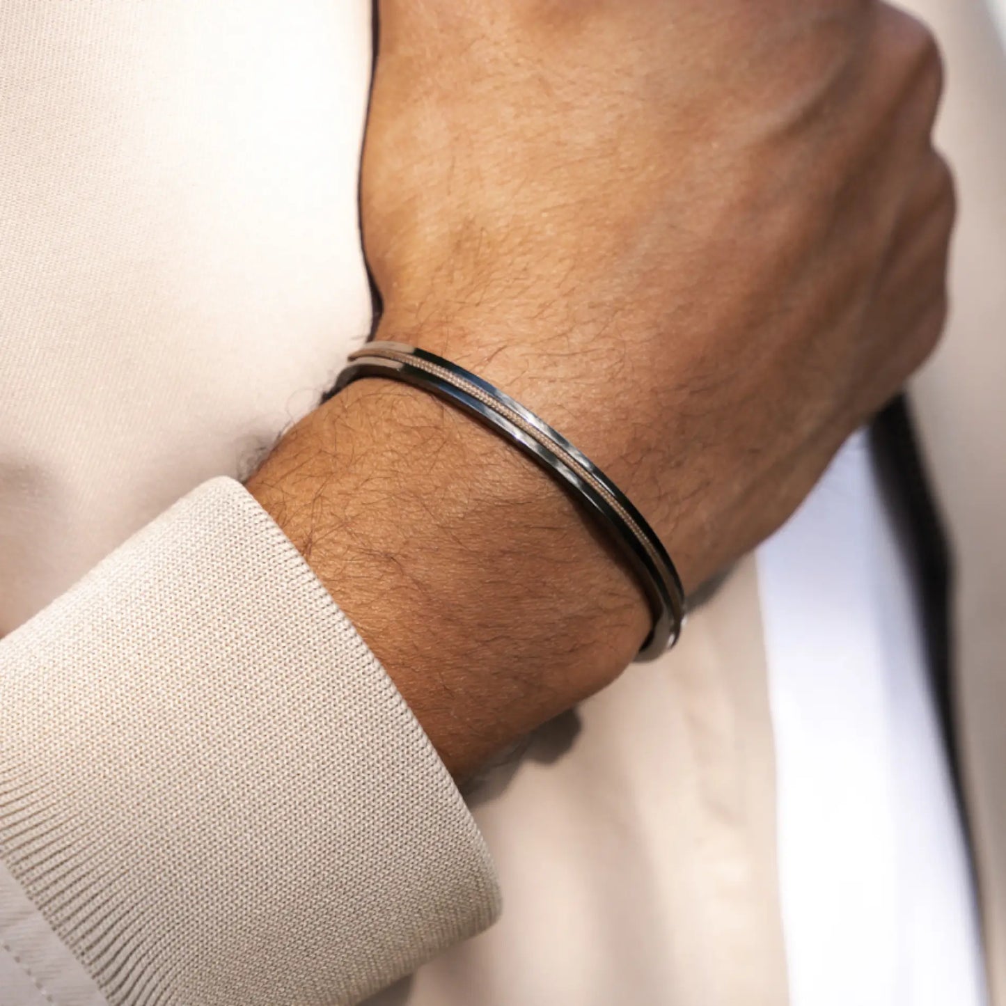Sand / Gunmetal || Slim metal bracelet with polished black and silver finishes worn on wrist over beige sleeve