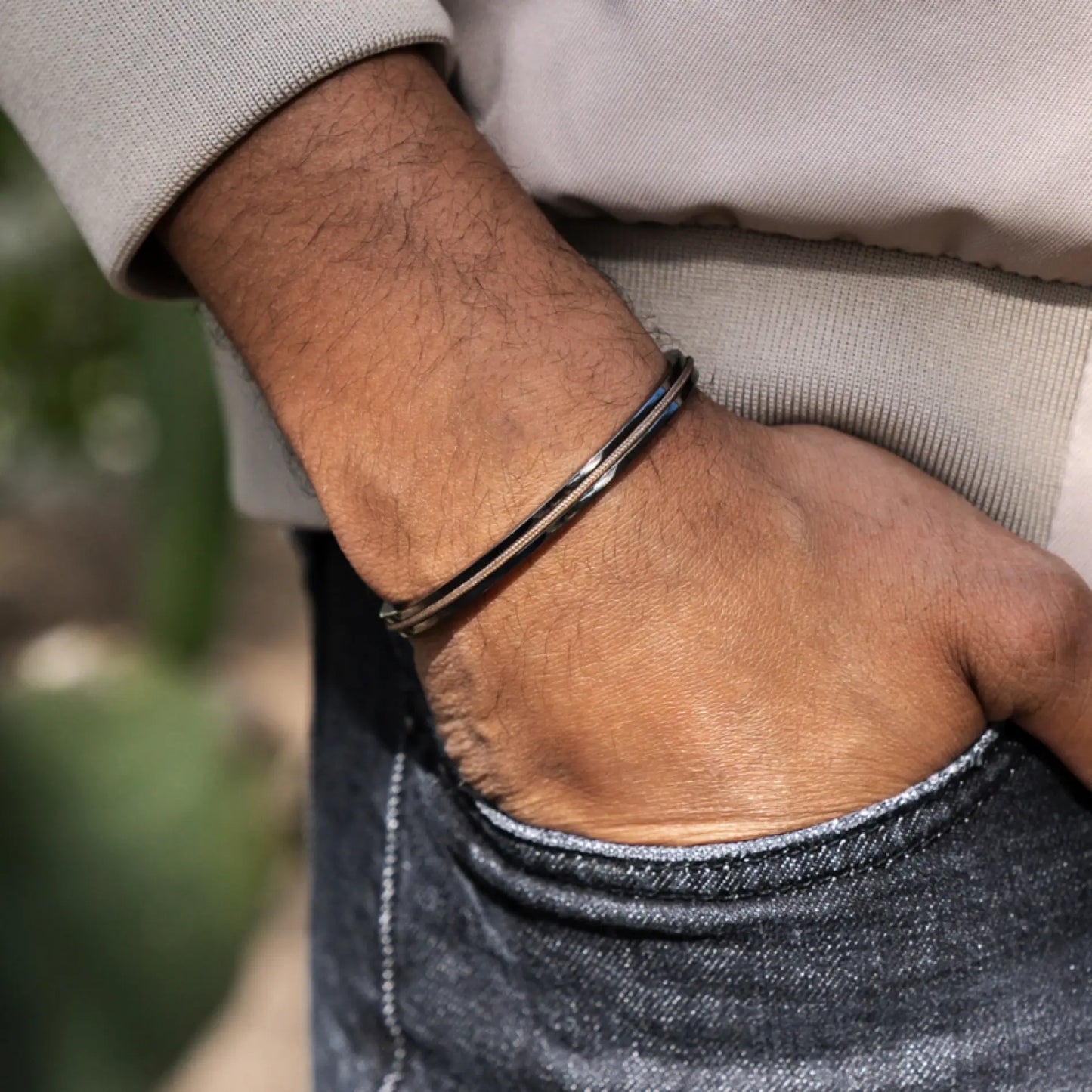 Gunmetal / Sand || Close up of a model wearing the Gunmetal Stainless Steel Adjustable Cuff Bracelet with Beige Nylon Rope in natural lighting. 