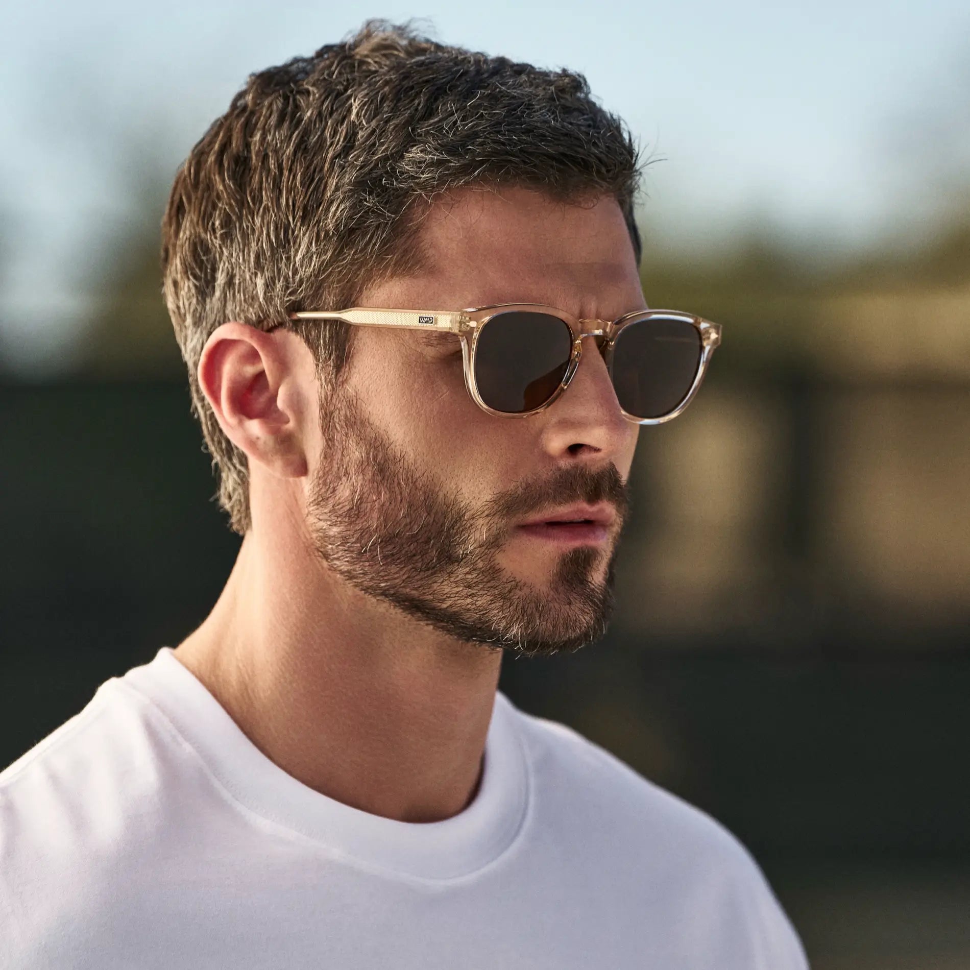 Man wearing Round Sunglasses with Sand Brown Frame and Dark Brown Oval Lens outdoors