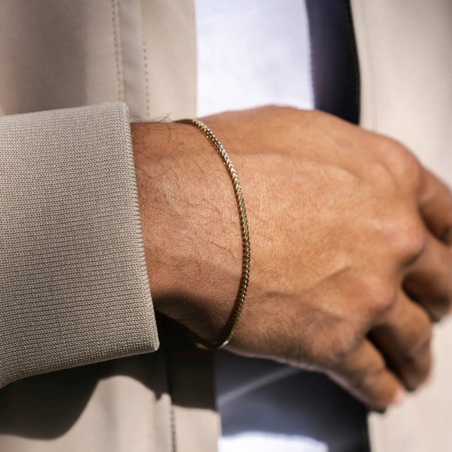 Gold || Close up of wrist wearing a slim gold chain bracelet paired with a beige blazer sleeve background