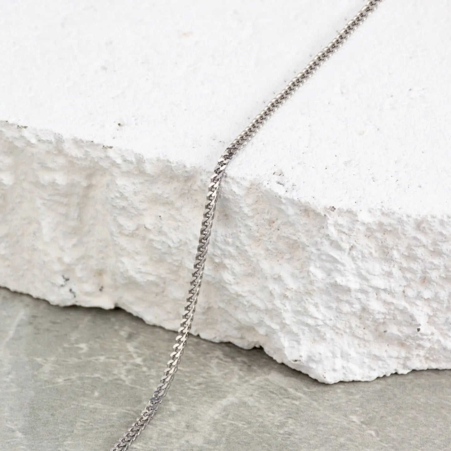 Silver || Close up of a finely detailed silver chain bracelet draped over textured white stone surface in natural light