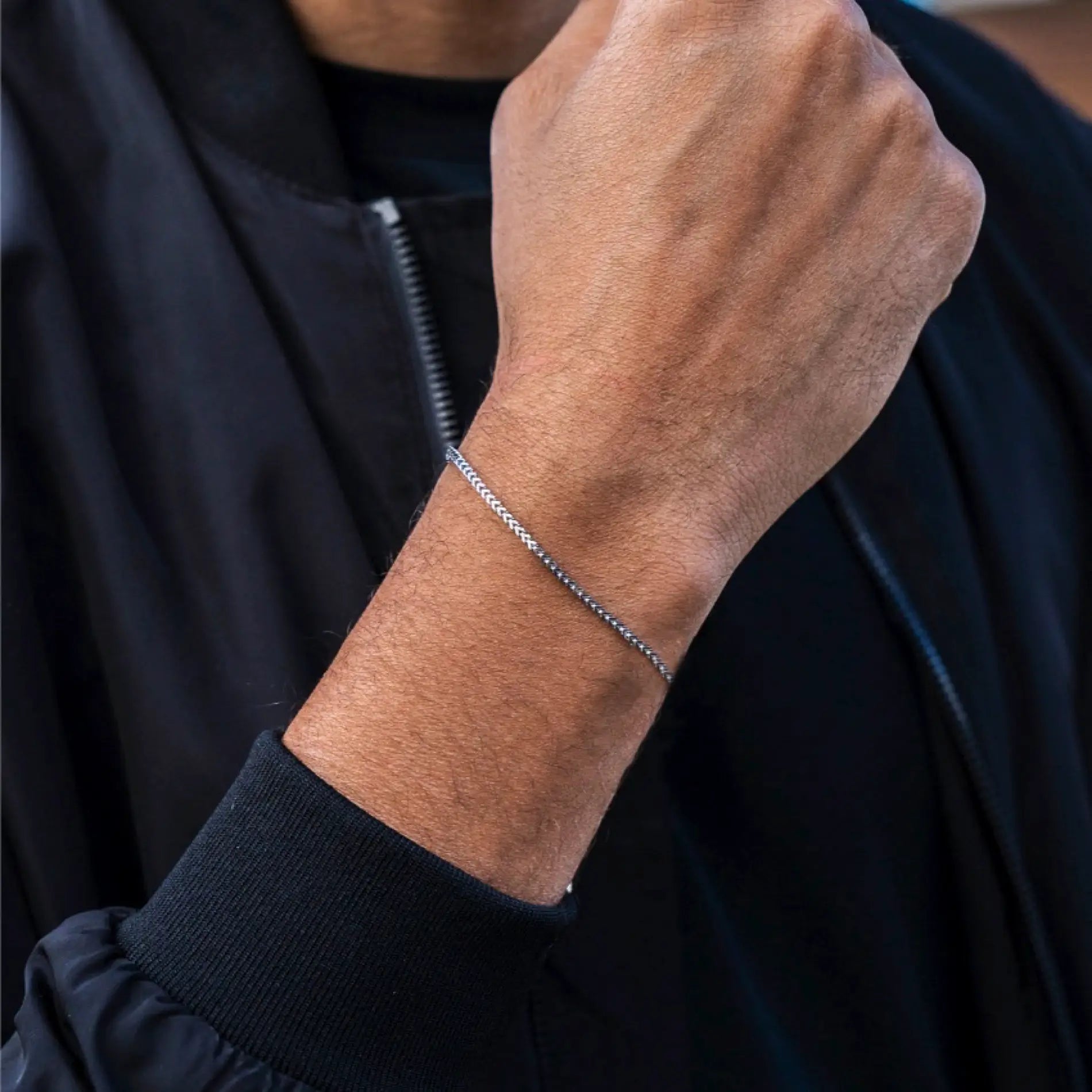 Silver || Slim silver chain bracelet worn on wrist over black long sleeve jacket in natural light