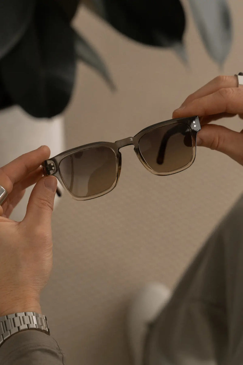 Hands holding Wayne sunglasses in Graphite Horizon Grey in a close-up lifestyle photo.