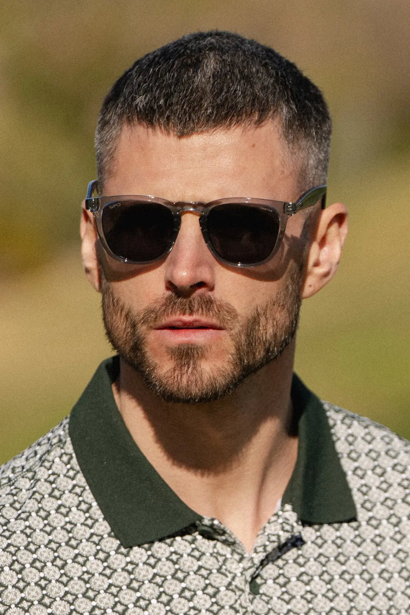 Man wearing translucent blue rectangular sunglasses with dark lenses outdoors.