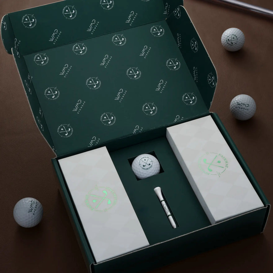 Open WMP Eyewear Fairway Collection gift box with green golf-motif interior packaging, two product boxes, a golf ball, and a tee, surrounded by WMP Eyewear golf balls