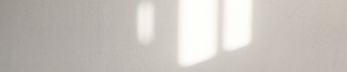 A close-up of a light beige or off-white textured surface with soft vertical white highlights or shadows.
