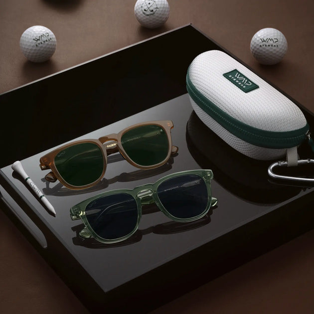 Wyndham style sunglasses in brown and green frames on a black tray with a golf-ball-print case, wooden tee, and WMP Eyewear golf balls